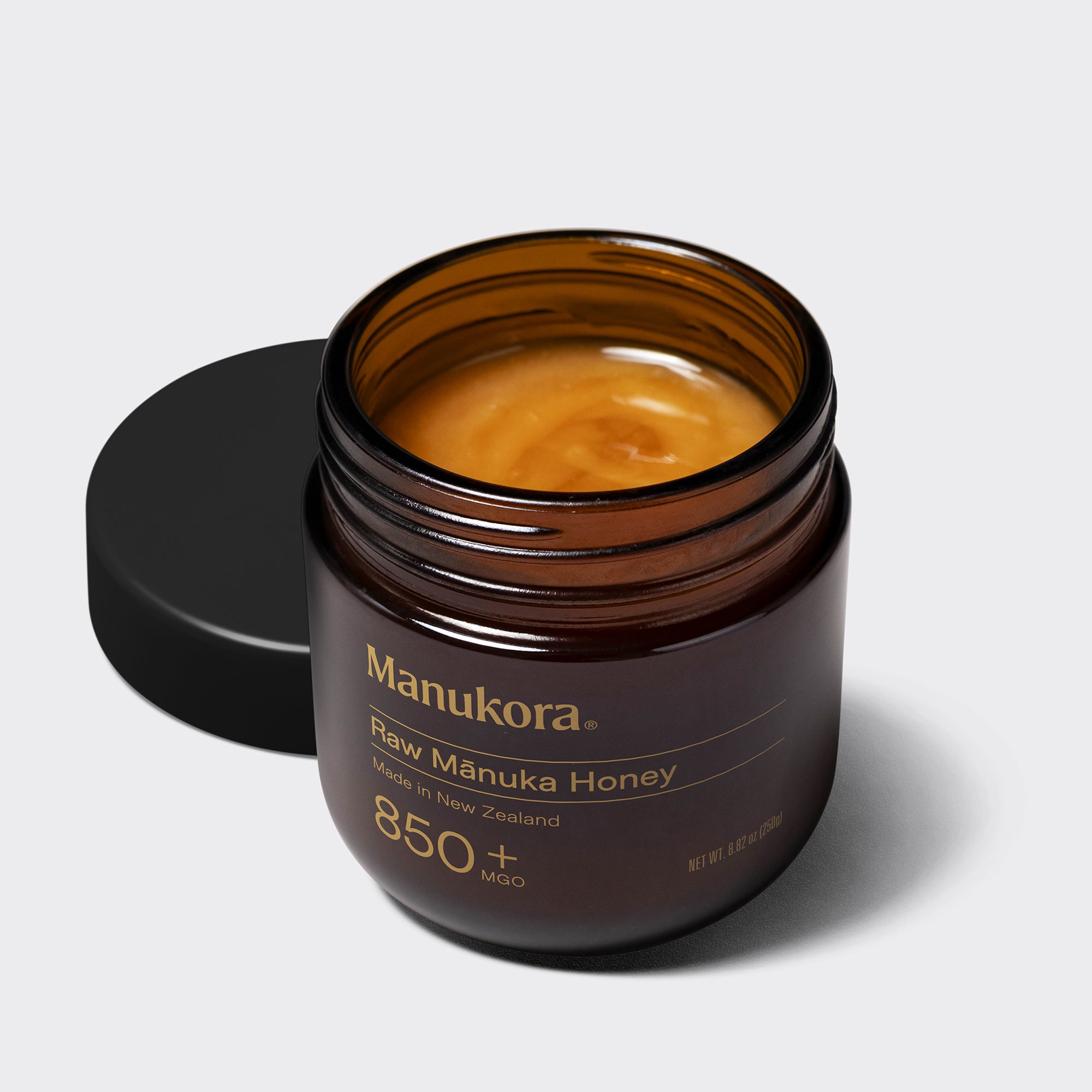 A hand holding a spoonful of Manukora raw Mānuka honey.