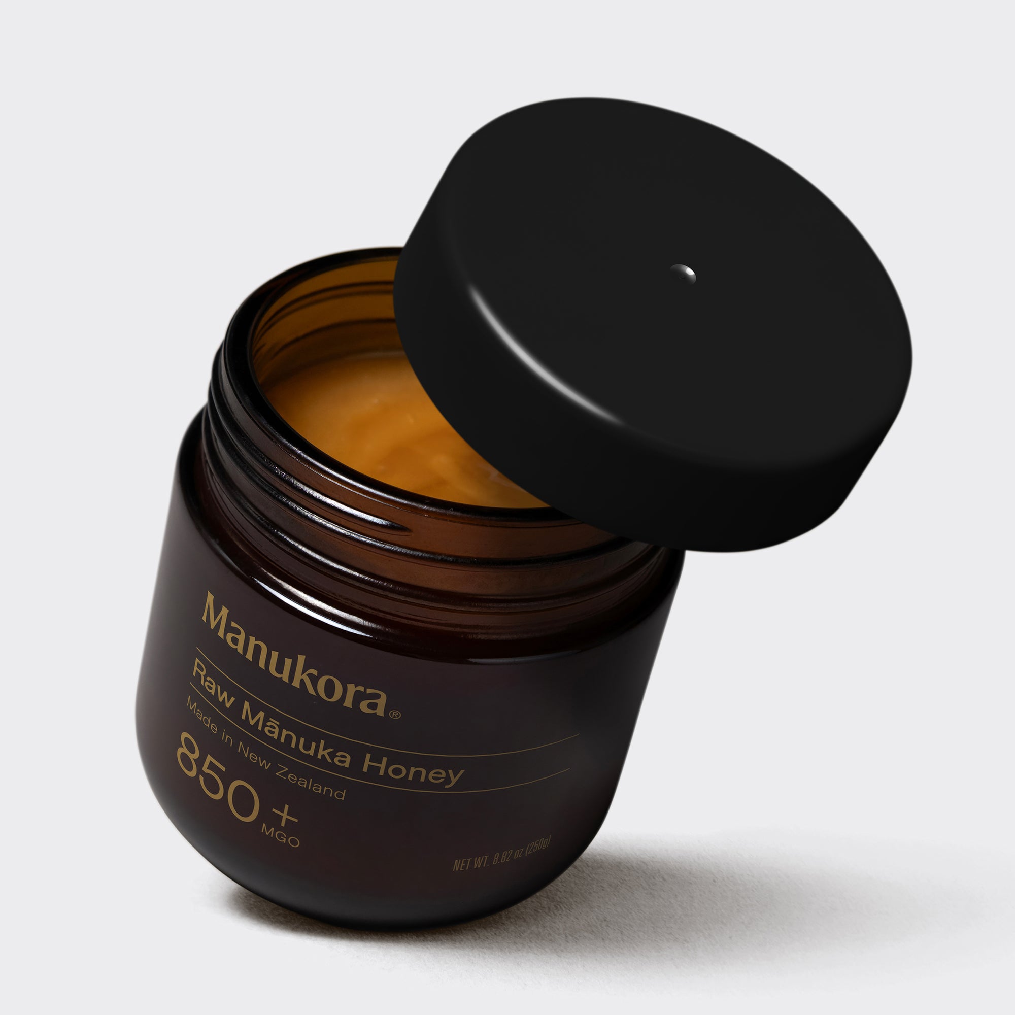 Hand drizzling Manuka honey onto a bowl of fresh berries and seeds.