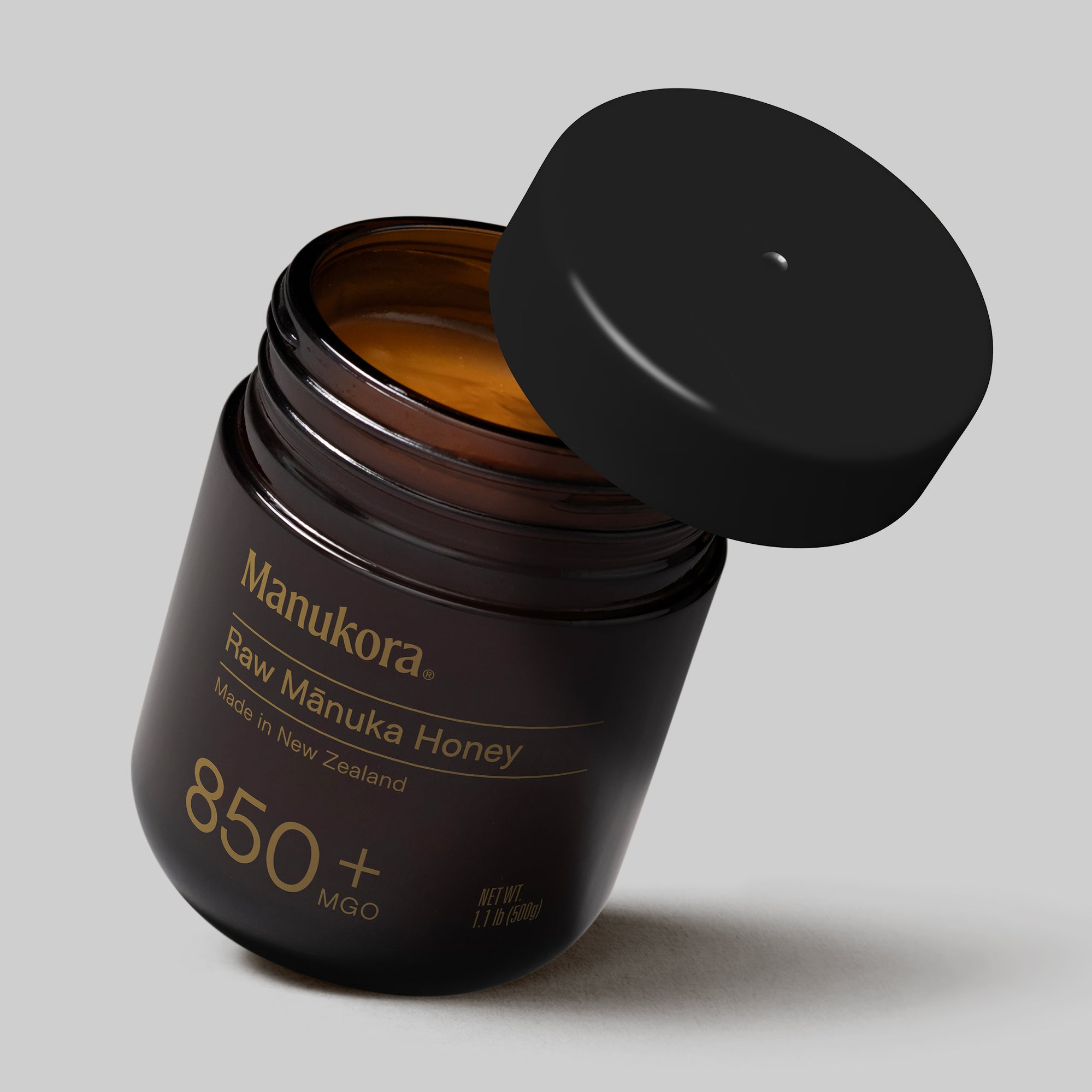 A hand holding a spoonful of Manukora raw Mānuka honey.