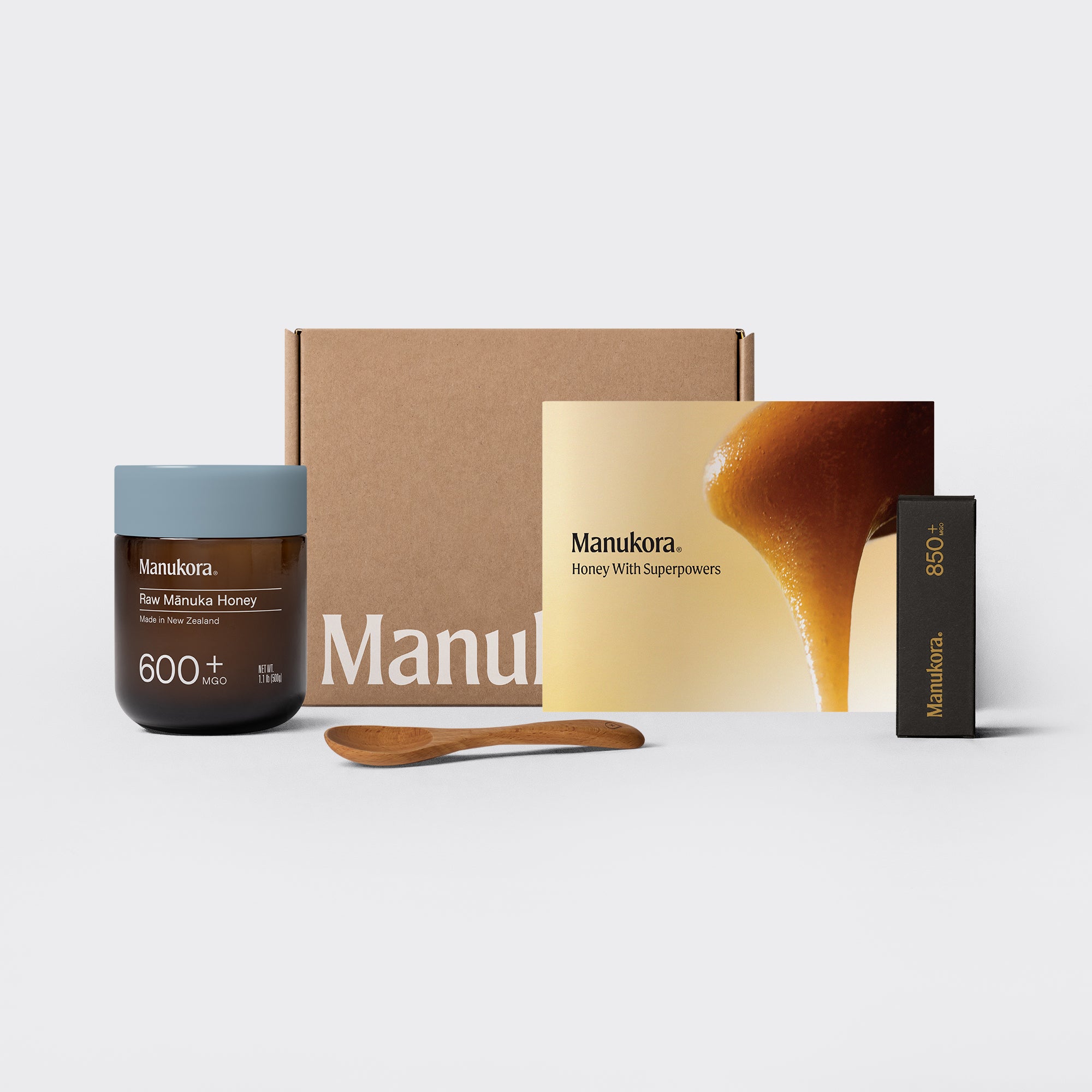 Set of Manukora raw Manuka honey products, including a jar, packaging box, spoon, and promotional card.