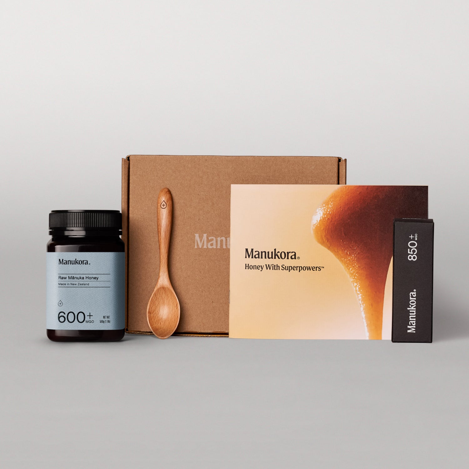 Set of Manukora raw Manuka honey products, including a jar, packaging box, spoon, and promotional card.