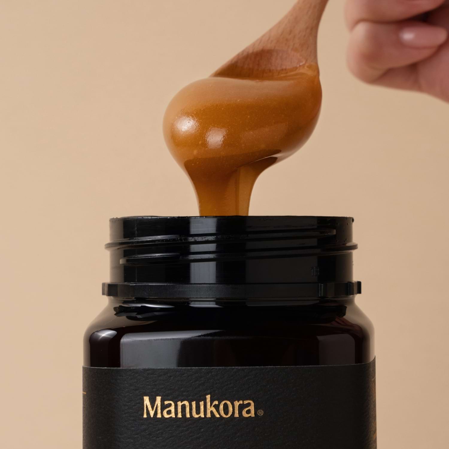 Person scooping Manukora raw Mānuka honey from a jar with a wooden spoon.