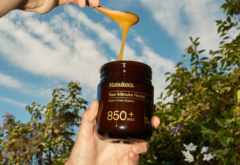 A hand holding a spoonful of Manukora raw Mānuka honey.