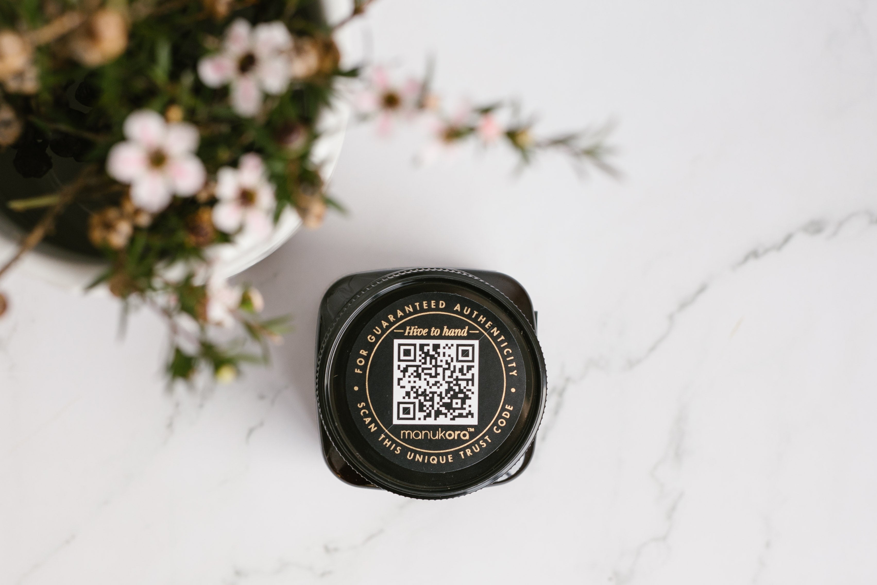 Manukora jar lid showing the batch QR code beside Mānuka blossom