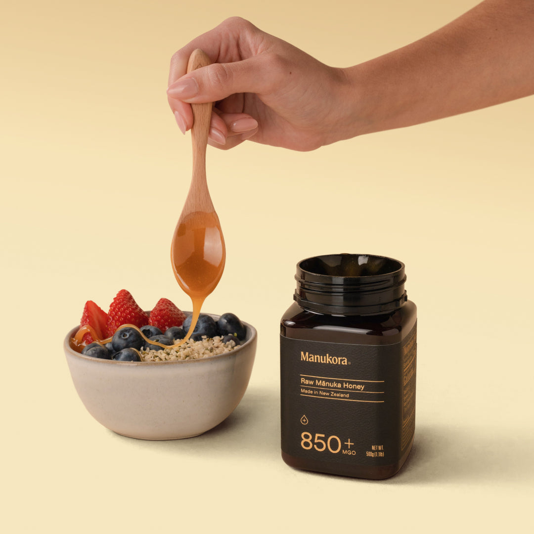 Hand drizzling Manuka honey onto a bowl of fresh berries and seeds.